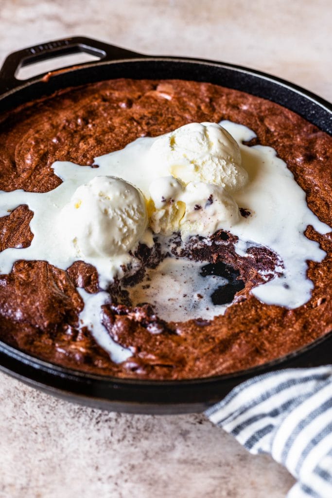brownies baked on a skillet, topped with ice cream with bites taken out of the brownies
