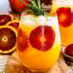 Blood orange cocktail served over ice, garnished with a rosemary sprig and fresh blood orange slices.
