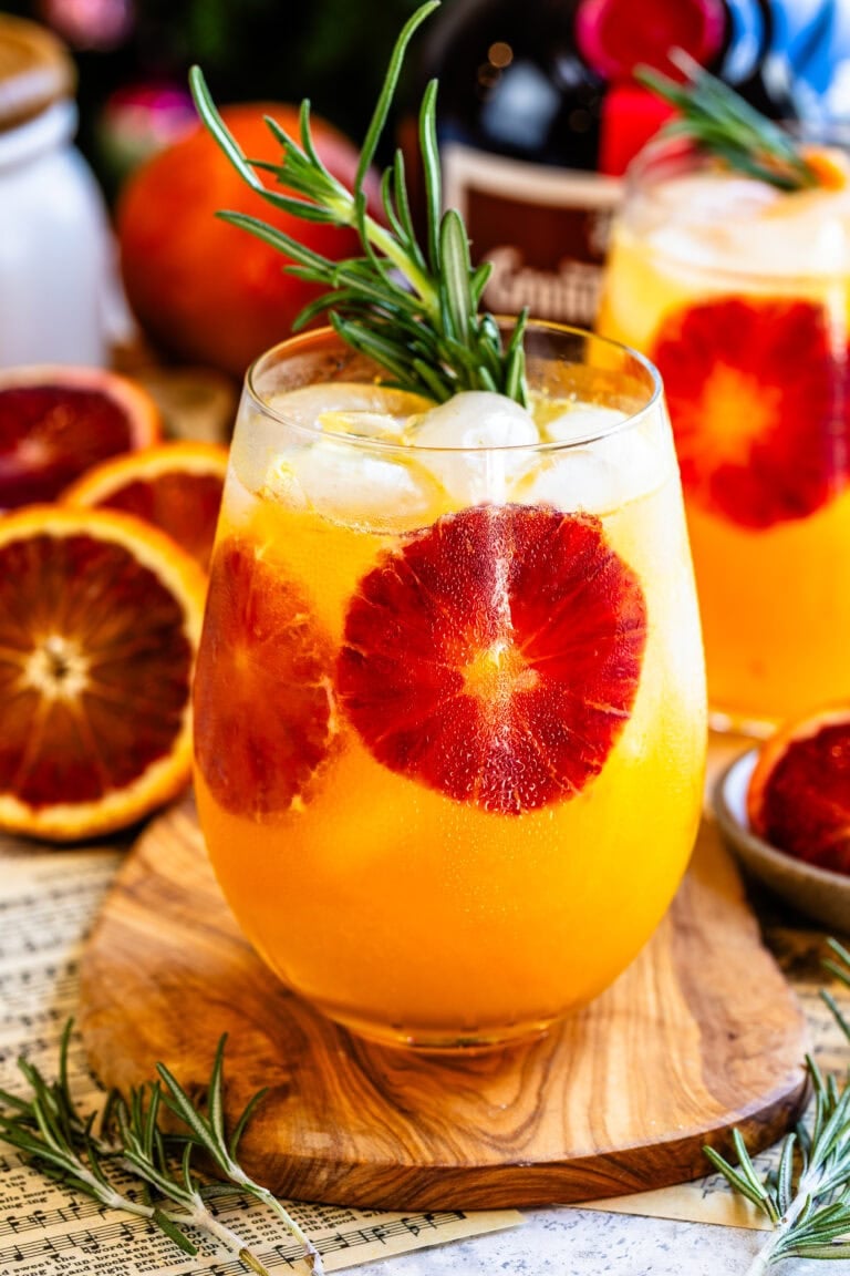 Blood orange cocktail served over ice, garnished with a rosemary sprig and fresh blood orange slices.