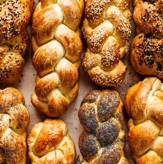 8 loaves of challah bread, some topped with sesame seeds, some plain and some topped with poppy seeds.