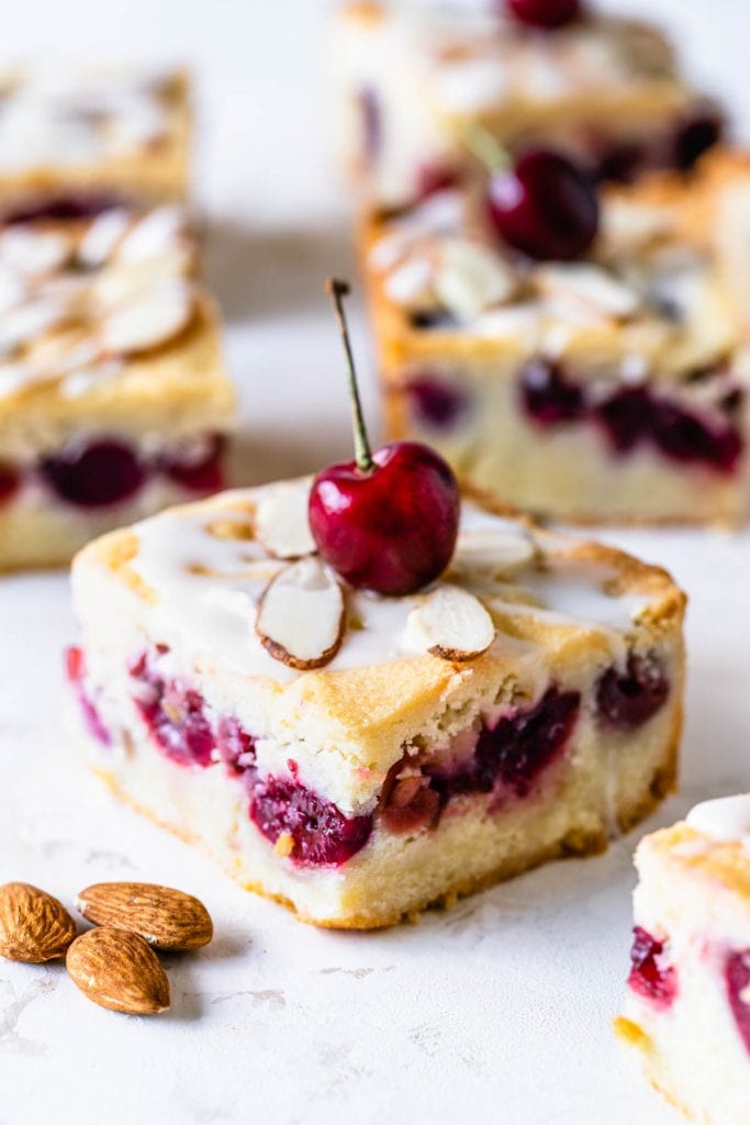 almond cherry bars topped with glaze and sliced almonds and fresh cherry