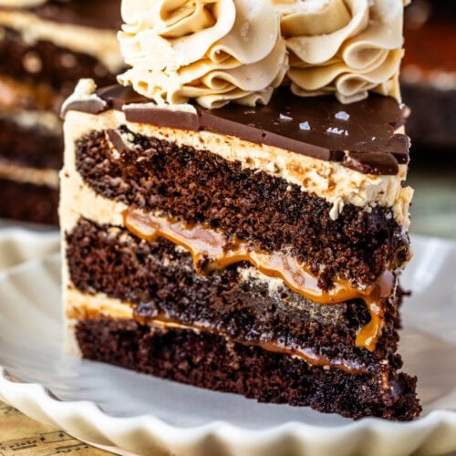 Slice of caramel Guinness chocolate cake with layers of chocolate cake, vanilla buttercream, and caramel filling, topped with chocolate ganache and salted caramel buttercream swirls.