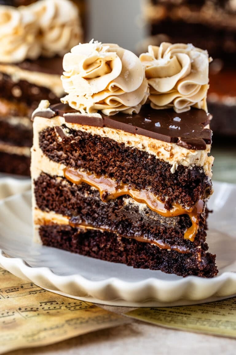 Slice of caramel Guinness chocolate cake with layers of chocolate cake, vanilla buttercream, and caramel filling, topped with chocolate ganache and salted caramel buttercream swirls.