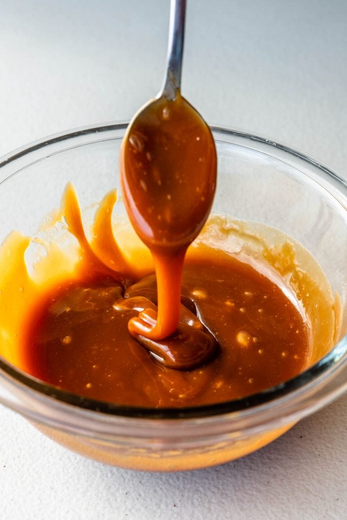 salted caramel sauce in a bowl with a spoon dripping with caramel sauce