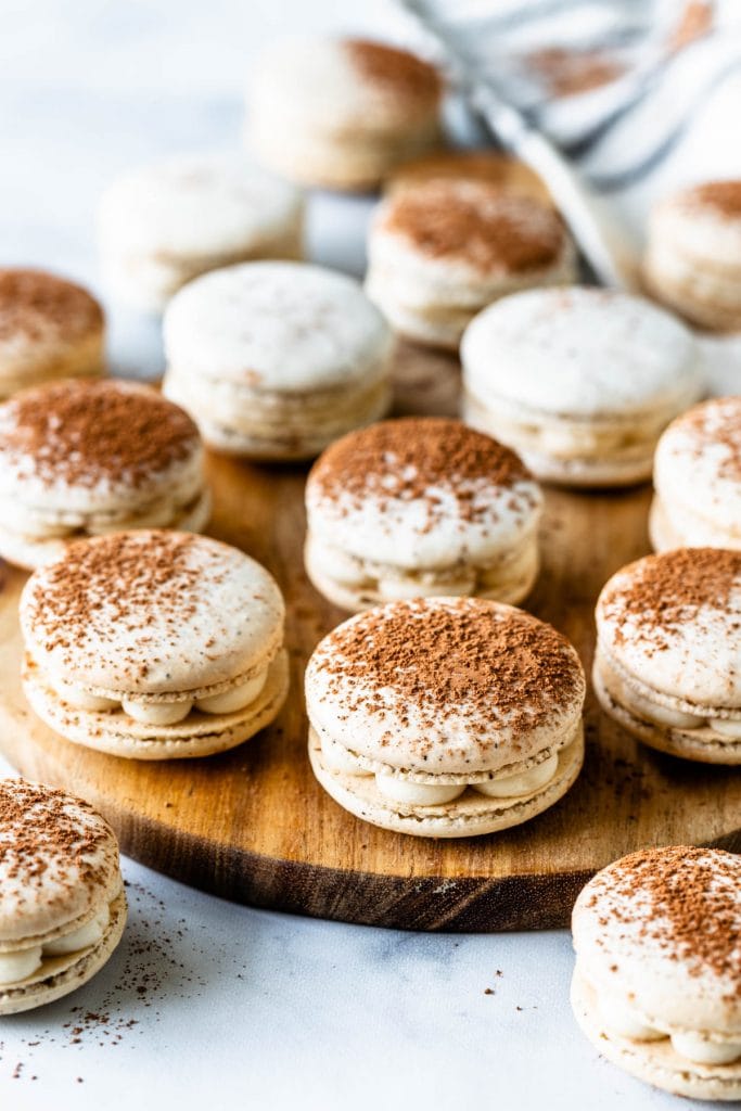 Tiramisu macarons in a box filled with mascarpone frosting, dusted with cocoa powder on top of a wooden board