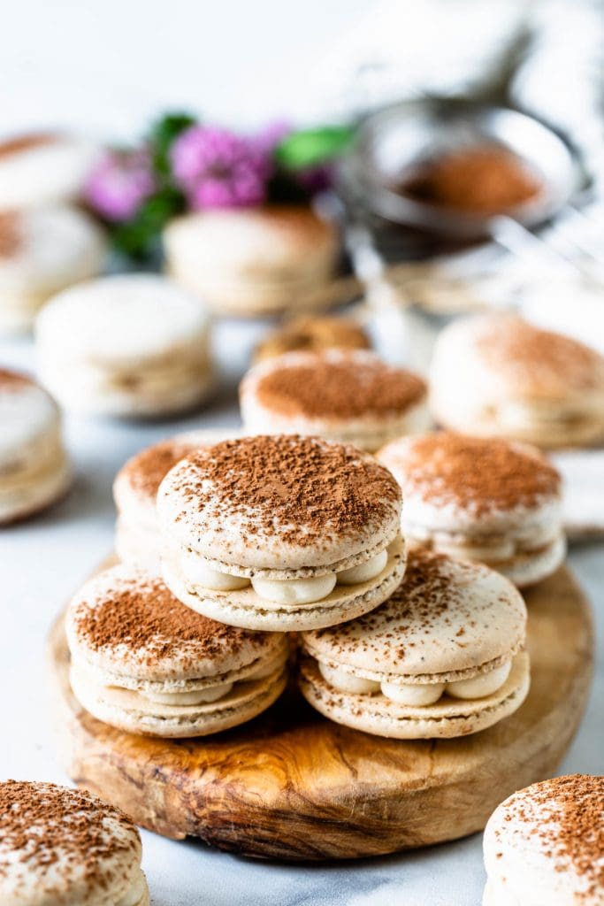 Tiramisu macaron filled with mascarpone frosting, dusted with cocoa powder on top of a wooden board