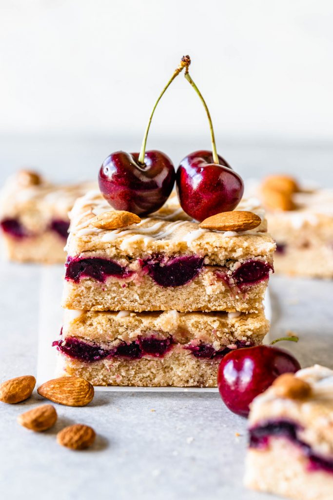 Almond Cherry Bars stacked on top of each other topped with two cherries