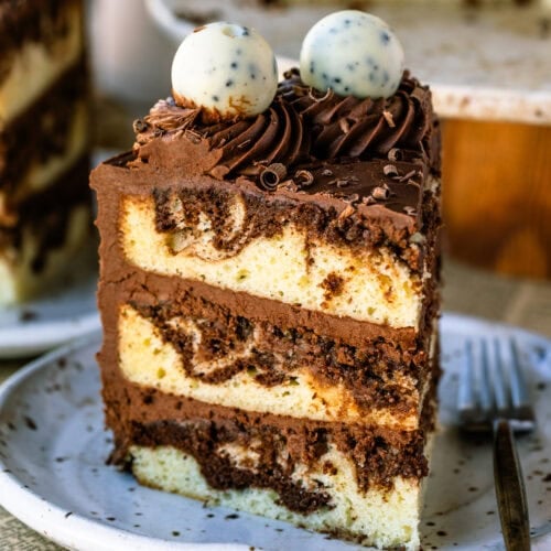 A slice of vanilla and chocolate marble cake with distinct swirls, layered with chocolate frosting and topped with piped swirls and chocolate truffles.