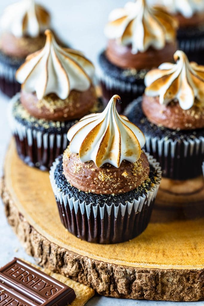 chocolate cupcakes topped with chocolate buttercream and toasted marshmallow, on top of a wooden board