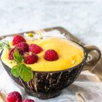 mango smoothie in a coconut bowl with raspberries on top