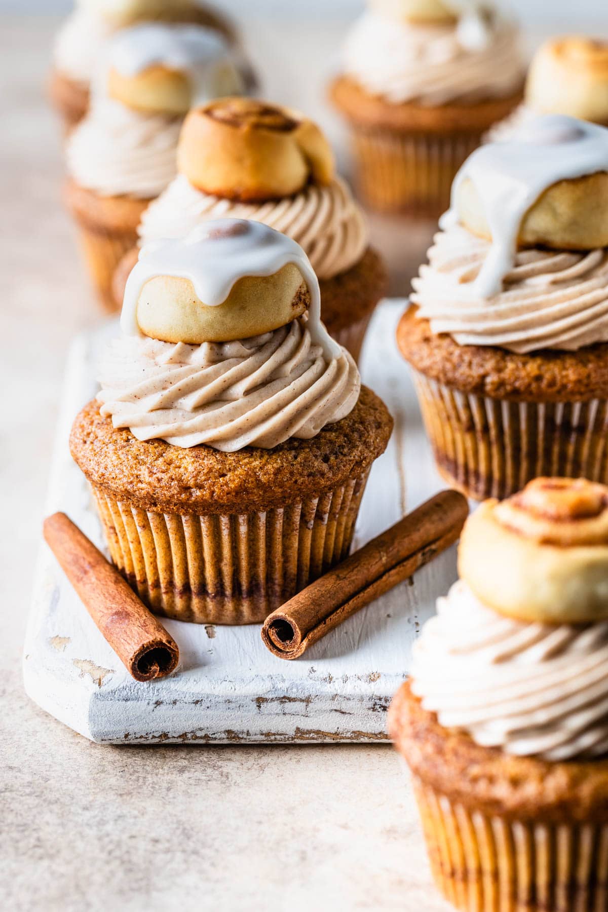 Cinnamon Roll Cupcakes topped with a glazed mini cinnamon roll with cinnamon sticks beside it.