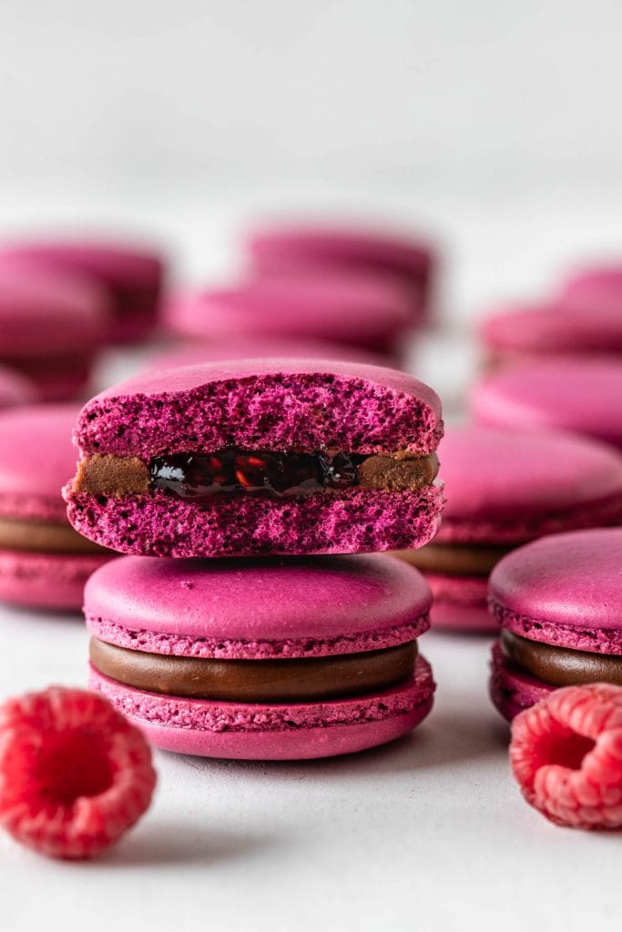 pink macarons filled with raspberry jam and chocolate ganache sliced in half showing the inside of the macarons.