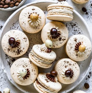 macarons topped with a coffee bean covered in chocolate, in a plate.