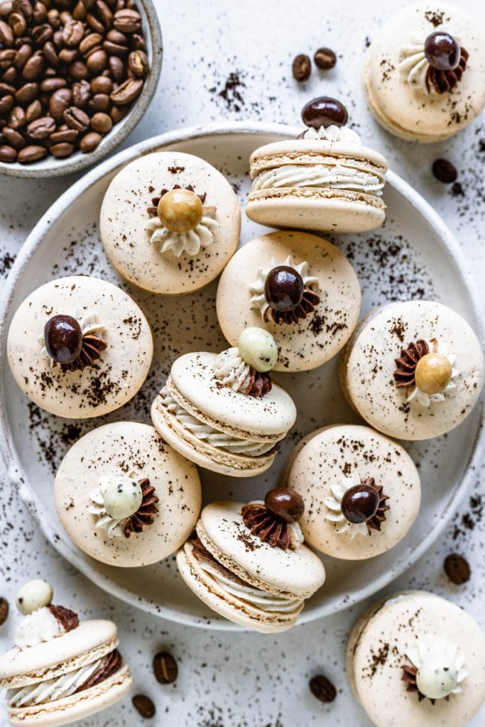 macarons topped with a coffee bean covered in chocolate, in a plate.