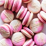 Strawberry macarons with two color shells drizzled with white chocolate and topped with graham cracker crumb.