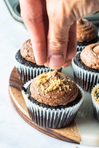 sprinkling graham cracker crumbs on top of smores cupcakes