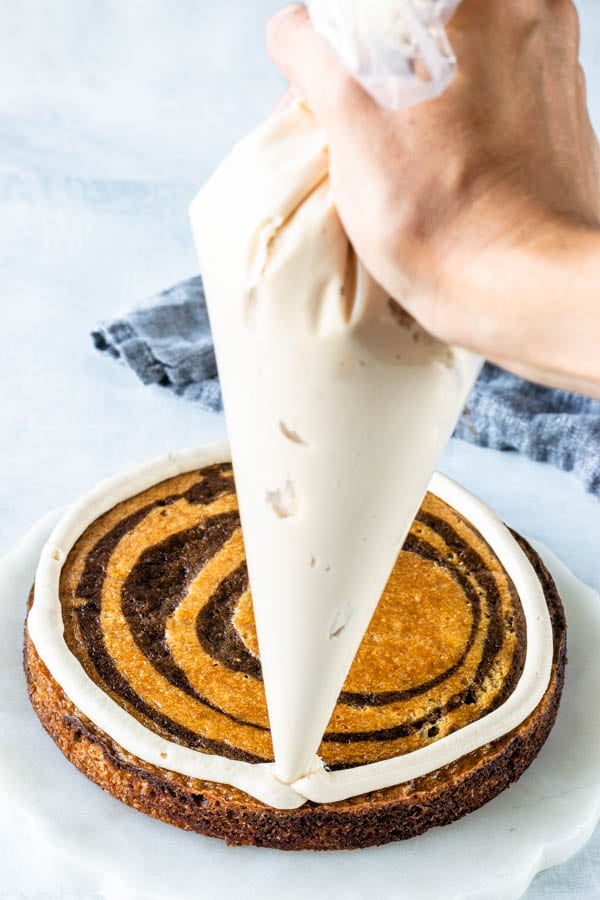 piping a ring of frosting around edges of marble cake