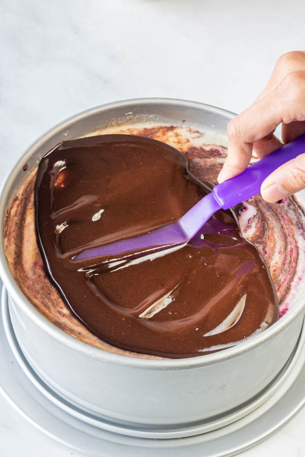 spreading chocolate sauce on top of cheesecake with an offset spatula