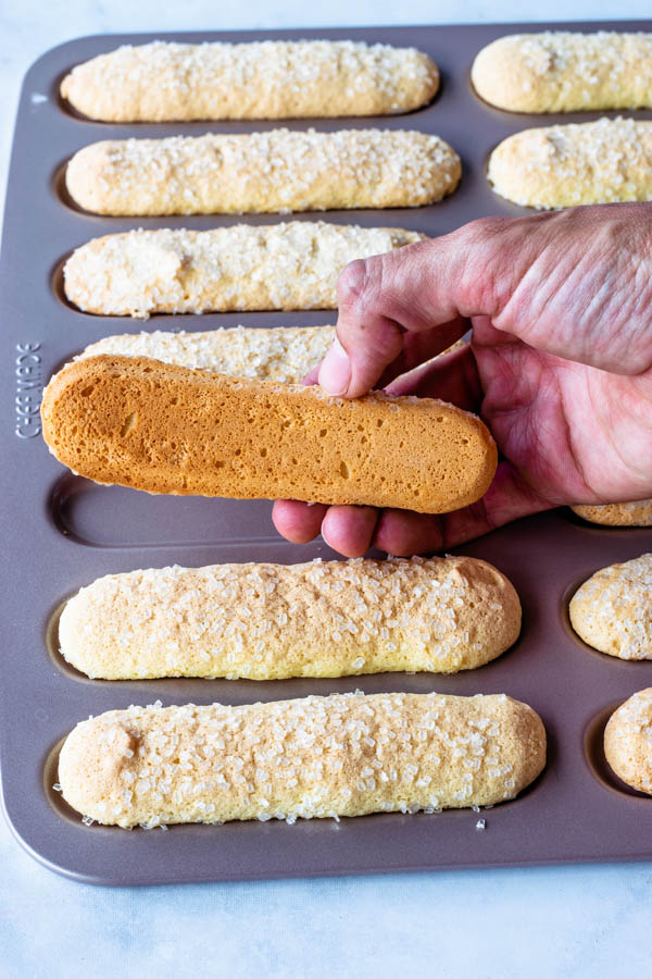 lifting a ladyfinger cookie off the pan to show the bottom