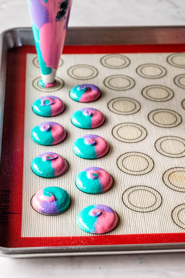 piping multi-colored macaron batter on silicon baking sheet