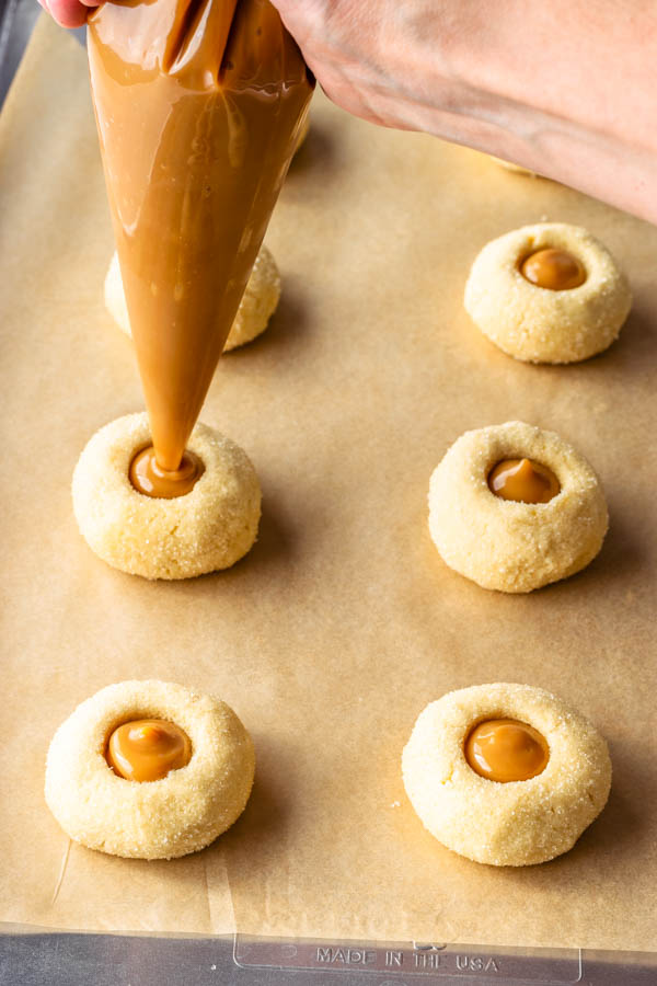 piping dulce de leche in the center of the thumbprint cookies