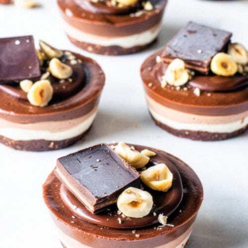 Mini vegan hazelnut cheesecakes with ombré chocolate layers, ganache, toasted hazelnuts, and chocolate pieces.