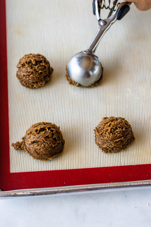 scooping vegan ginger cookie dough onto baking sheet with silicon mat