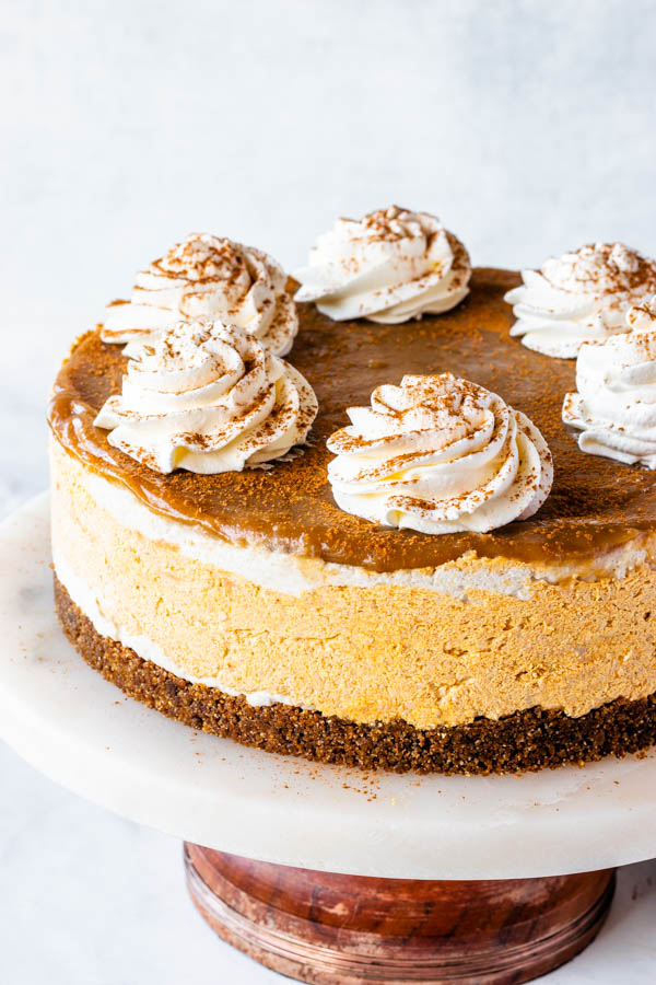 vegan pumpkin cheesecake with caramel sauce on top and whipped coconut cream and a sprinkle of pumpkin spice
