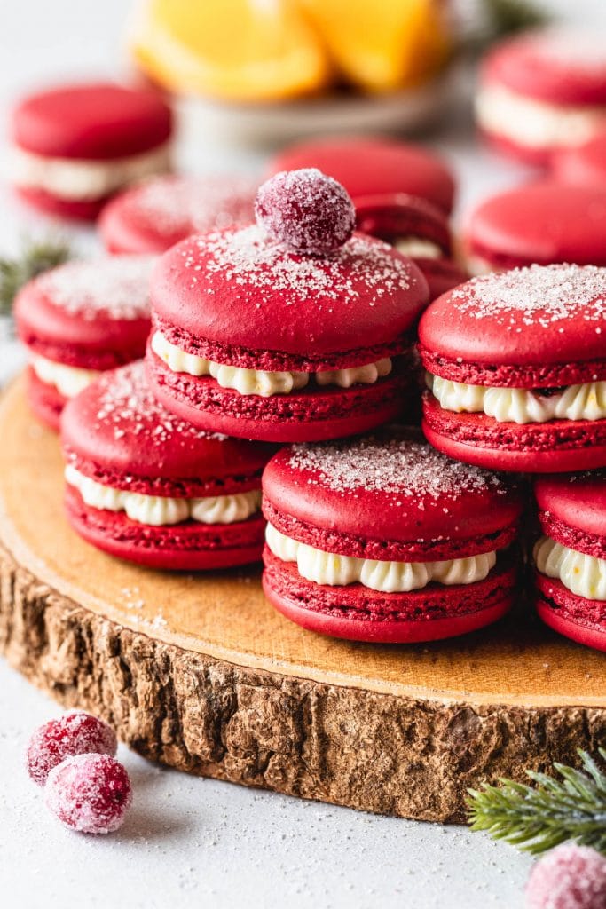 cranberry macarons with dusting of sugar on top, on top of a wooden board topped with sugared cranberry.