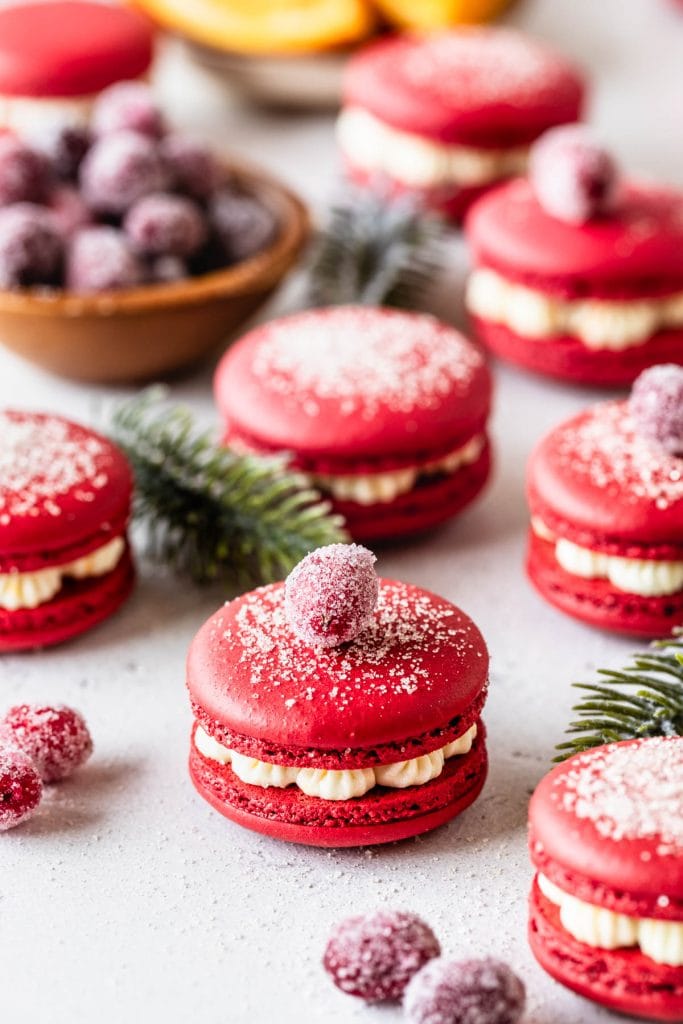 cranberry macarons topped with sugar and with sugared cranberries, filled with orange buttercream.