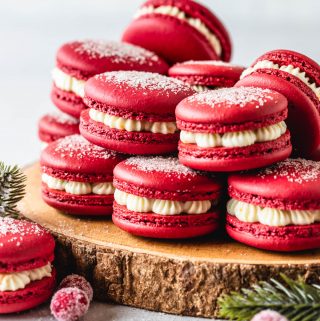 cranberry macarons with dusting of sugar on top, on top of a wooden board.