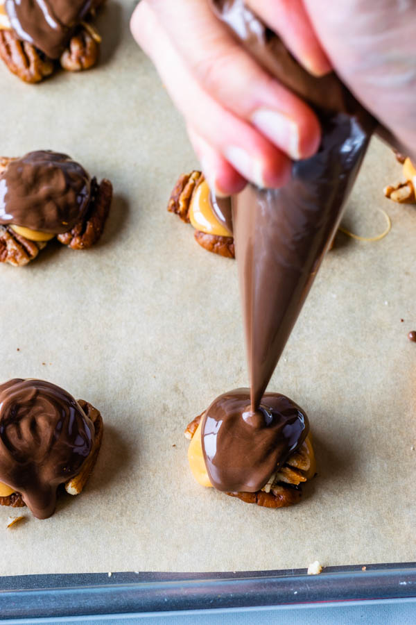 piping chocolate over pecan caramel clusters