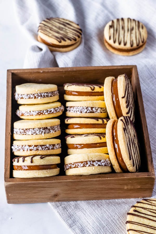 Alfajor Cookies filled with dulce de leche drizzled with melted chocolate and coated in coconut