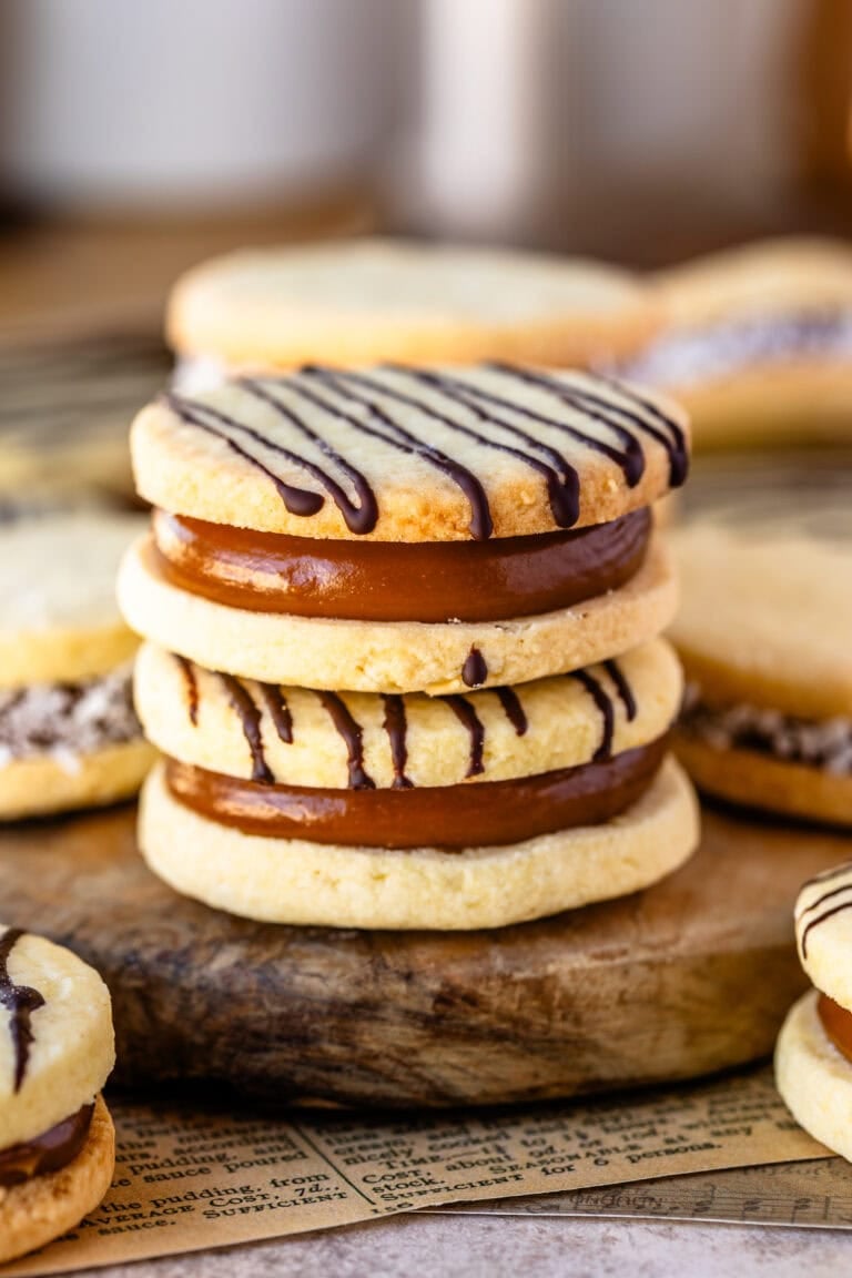 Finished alfajor cookies filled with dulce de leche and drizzled with chocolate, arranged on a wooden board.