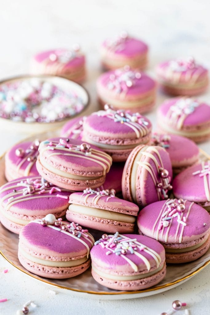 Champagne Macarons pink macarons topped with a drizzle of white chocolate and sprinkles.