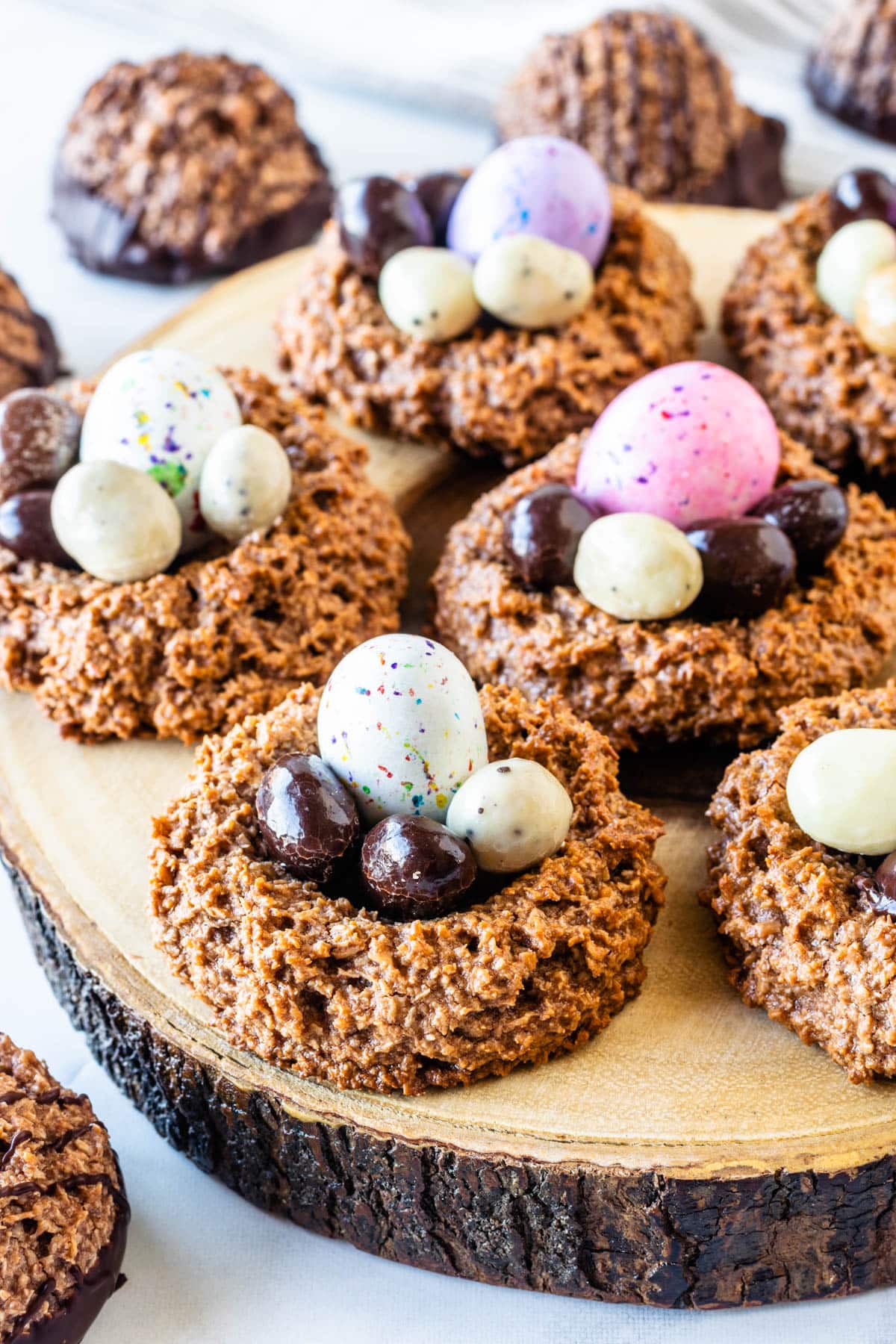 Chocolate coconut macaroon Easter nests filled with assorted chocolate egg candies on a rustic wood serving board.
