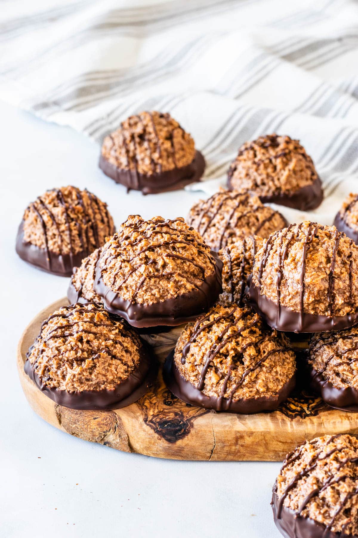 Chocolate coconut macaroons with chocolate-dipped bottoms and chocolate drizzle piled on a rustic wooden serving board.