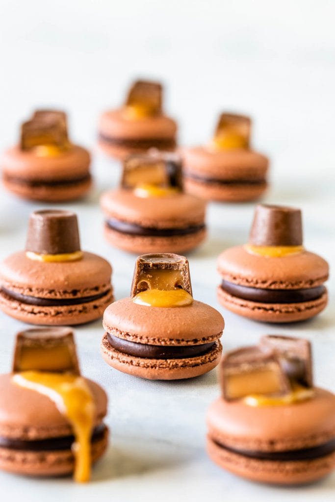 Chocolate Caramel Macaron in the front filled with caramel and chocolate topped with a rolo candy and caramel sauce