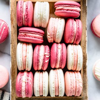 Pink, white, and dark pink strawberry rhubarb macarons in a box, from a bird's eye view, with jam in the top right corner