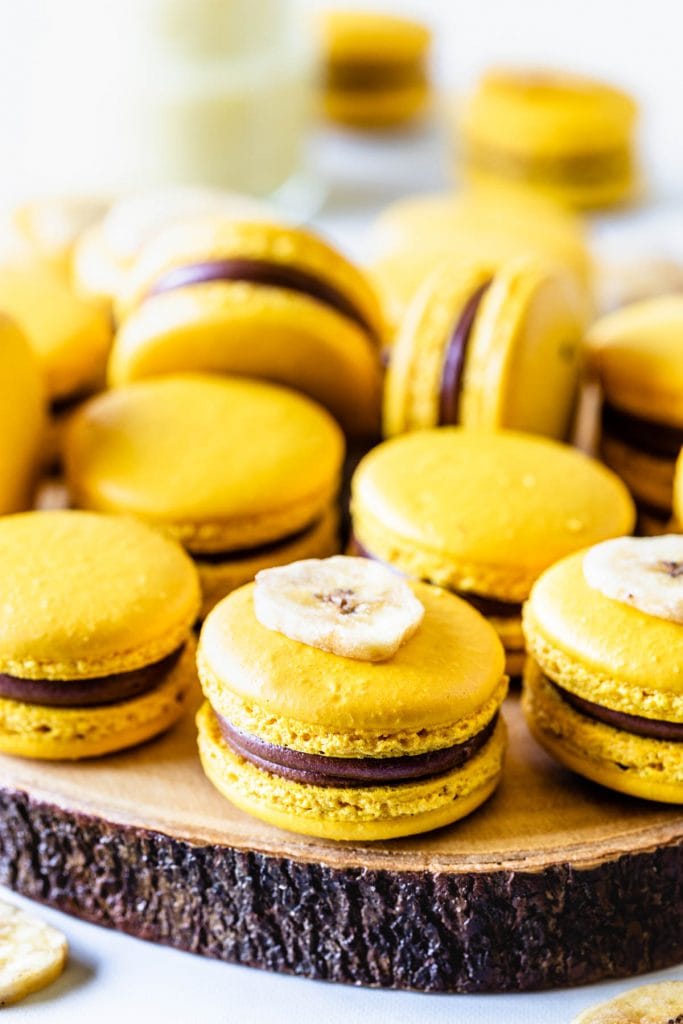 Banana Macarons yellow macarons in a box with chocolate and banana pudding filling on top of a wooden board