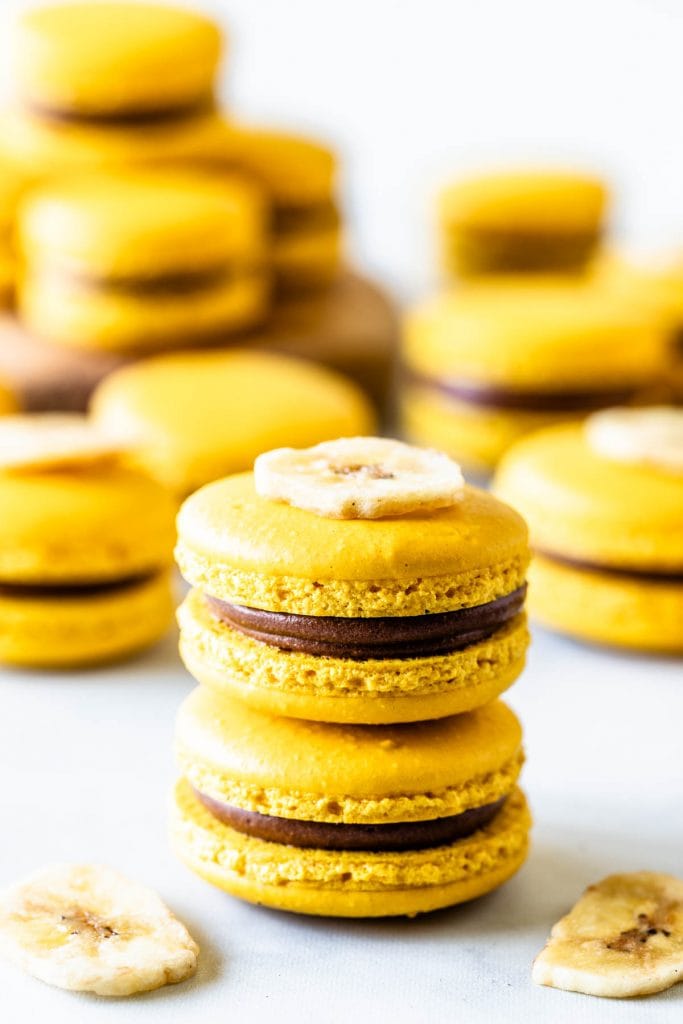stacked yellow macarons with chocolate filling and a dried banana chip on top