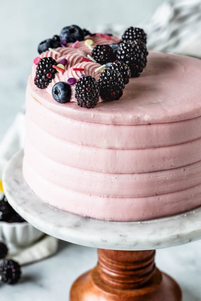 Lemon Blackberry Cake pink cake topped with blackberries and blueberries, on a cake stand