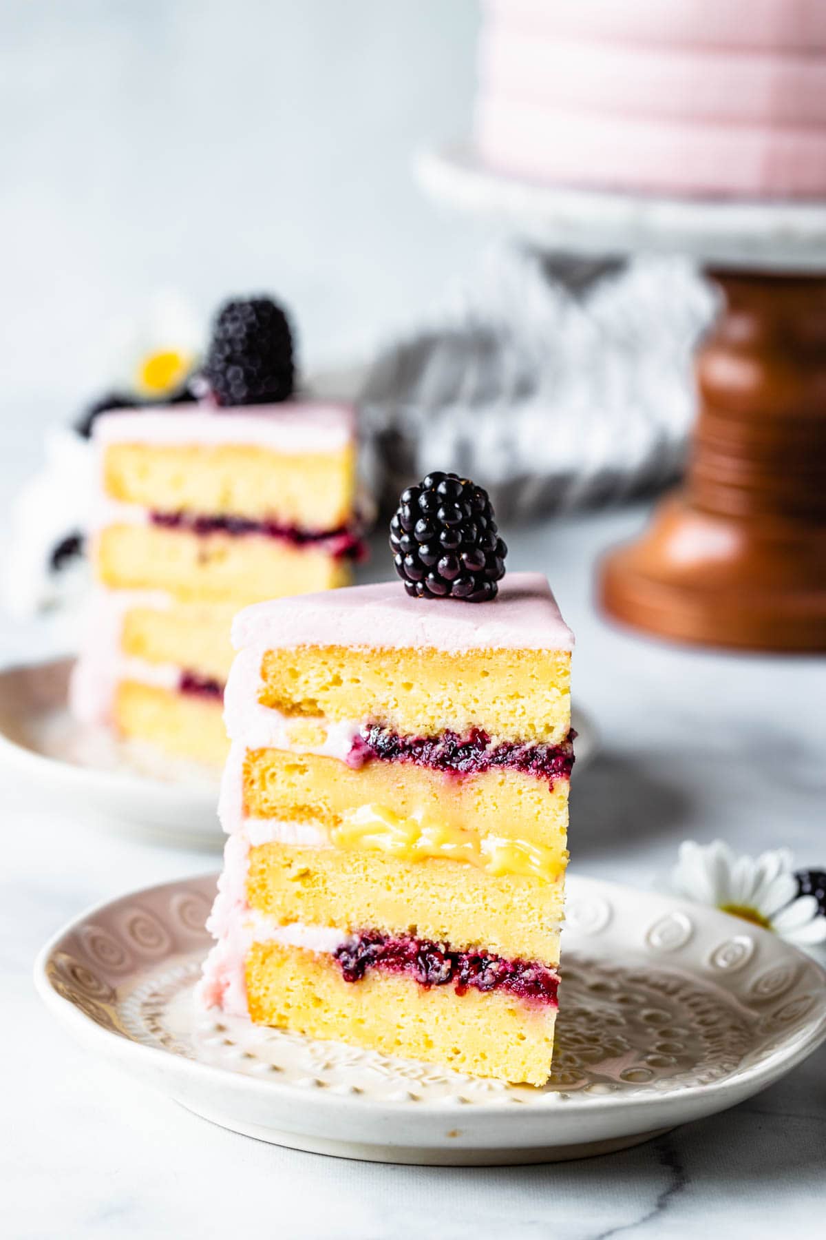 Lemon Blackberry Cake slice showing the top and bottom filling of blackberry jam, and the middle filling is lemon curd, covered in a pink blackberry buttercream