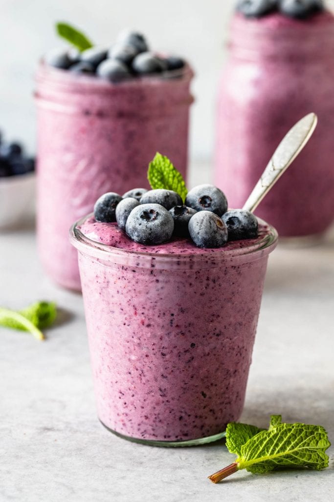 blueberry slushie in a mason jar topped with mint leaf and frozen blueberries and a spoon