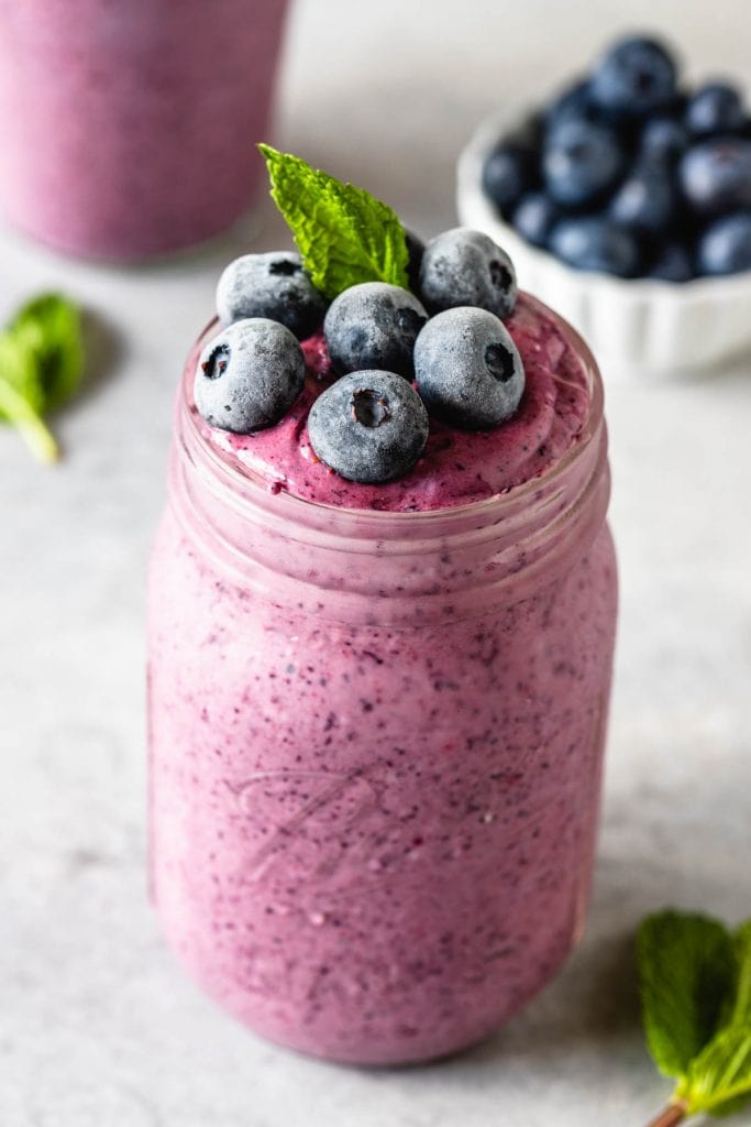 blueberry slushie in a mason jar topped with mint leaf and frozen blueberries and a spoon