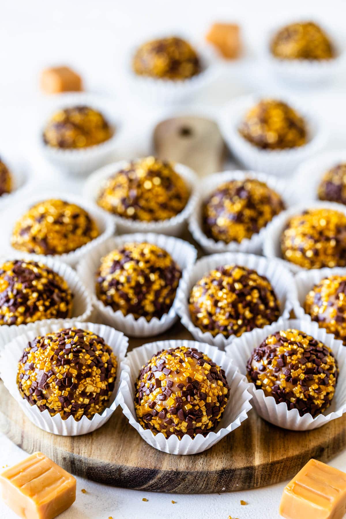 Caramel Fudge balls coated in golden flakes and chocolate flakes on top of a wooden board