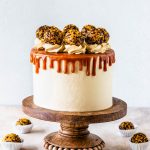 Salted Caramel Chocolate Cake covered with caramel drip and caramel truffles on a wooden cake stand