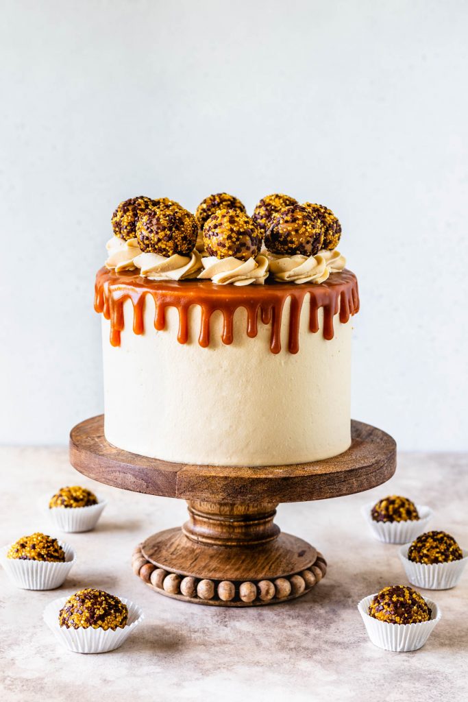 Salted Caramel Chocolate Cake covered with caramel drip and caramel truffles on a wooden cake stand