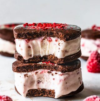 Chocolate Raspberry Ice Cream Sandwiches with a bite taken out, two sandwiches stacked. topped with chocolate drizzle and freeze dried raspberries