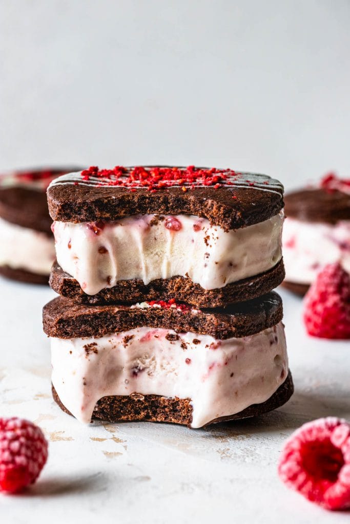 Chocolate Raspberry Ice Cream Sandwiches with a bite taken out, two sandwiches stacked. topped with chocolate drizzle and freeze dried strawberries